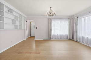 Spare room featuring arched walkways, light wood finished floors, suspended lighting, and built in shelves