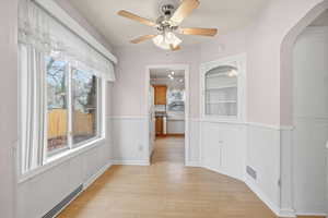 Unfurnished dining area with arched walkways, light wood-style floors, a ceiling fan, and wainscoting