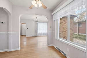 Hallway featuring wainscoting, a chandelier, arched walkways, and light wood finished floors