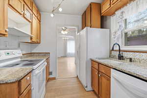 Kitchen featuring white appliances, wood finish cabinets, light wood-style floors, light stone countertops, and ceiling fan