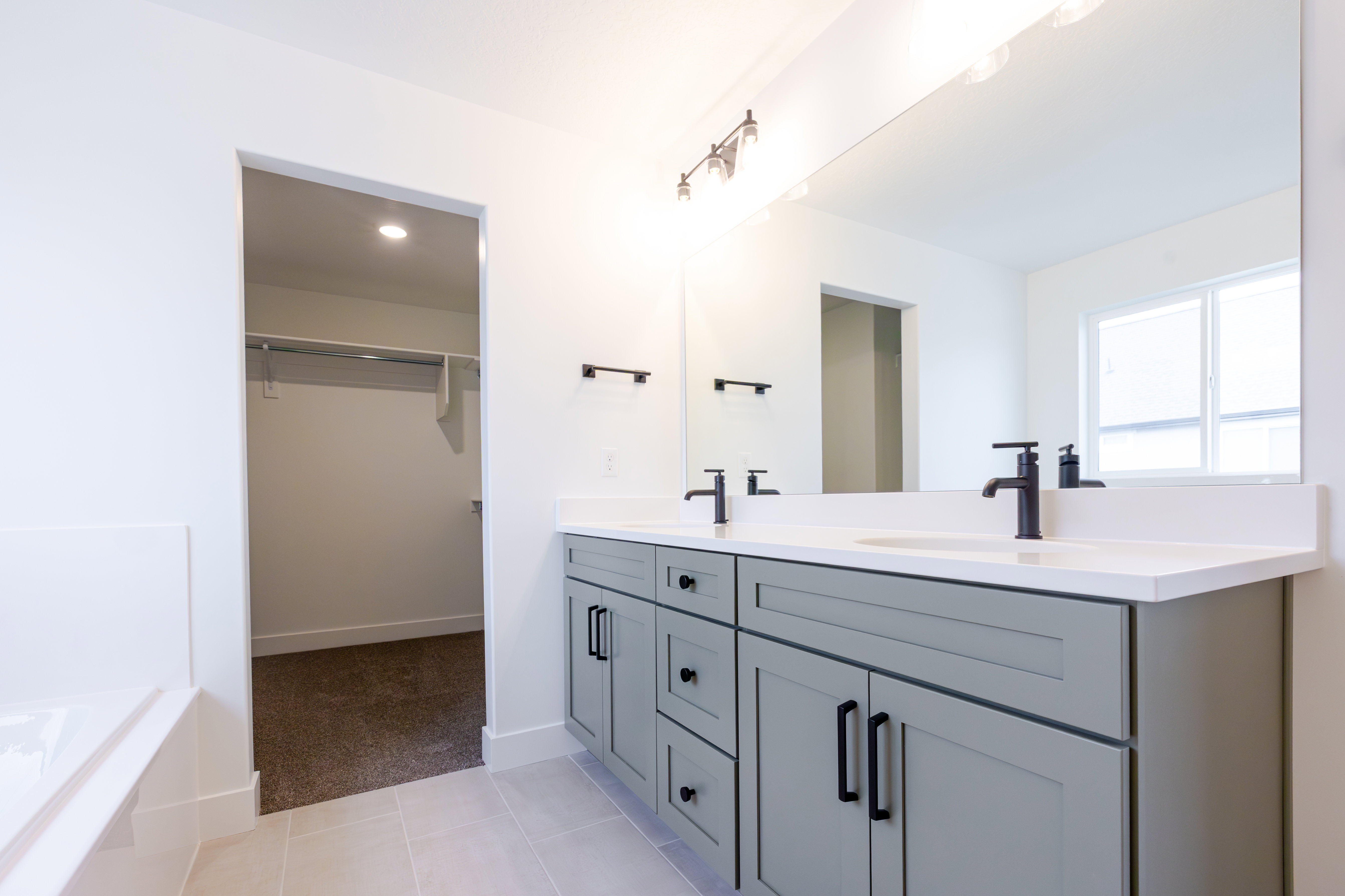 Dual vanity featuring light gray cabinetry with black hardware, white countertops, and matte black fixtures