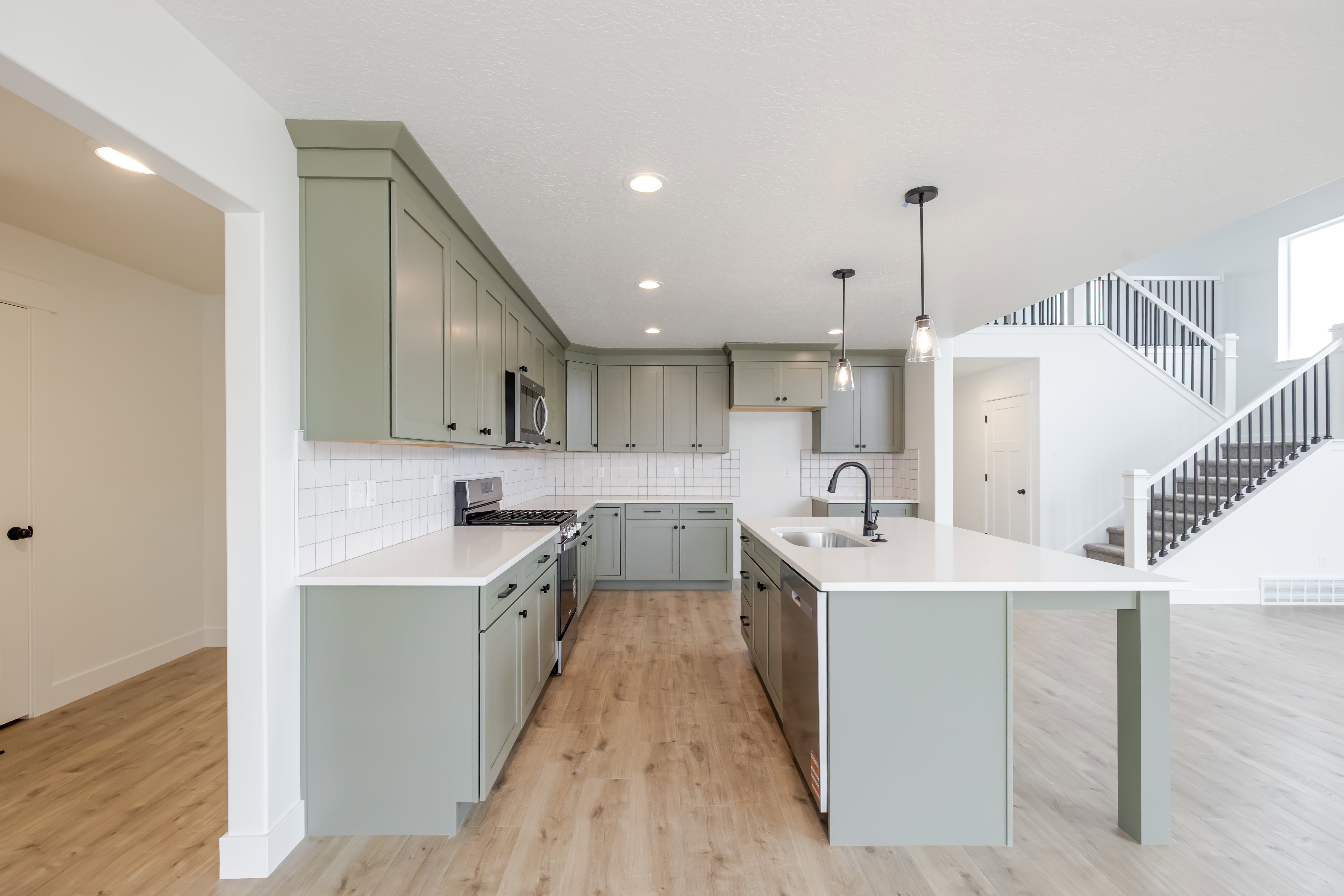 Open-concept kitchen featuring light green cabinetry, white countertops, subway tile backsplash, and wood-finish flooring