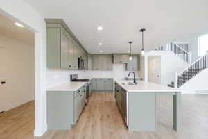 Open-concept kitchen featuring light green cabinetry, white countertops, subway tile backsplash, and wood-finish flooring
