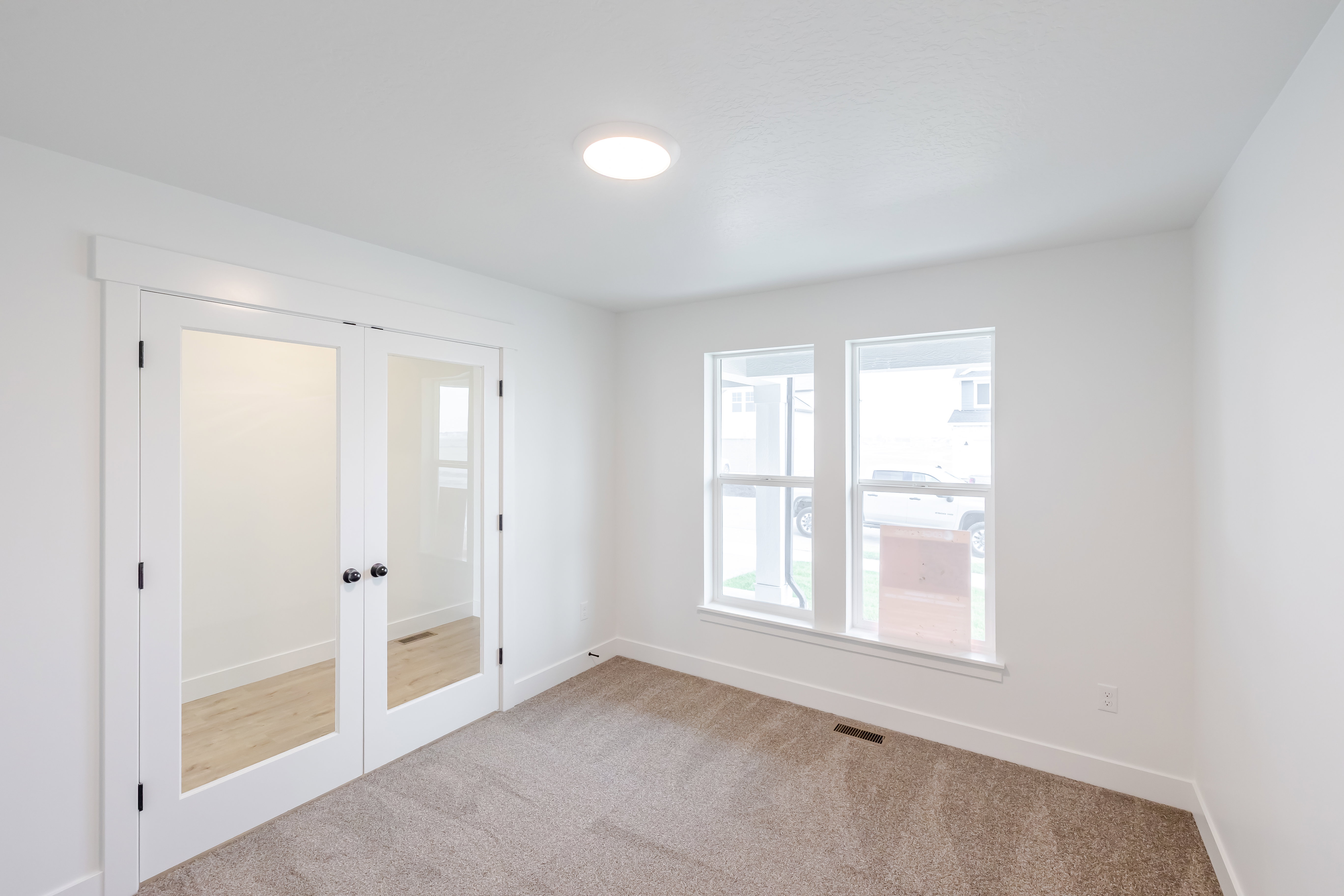 Room with French doors featuring frosted glass panels, two windows with white trim, recessed ceiling lighting, and carpet flooring