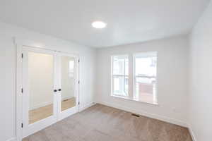 Room with French doors featuring frosted glass panels, two windows with white trim, recessed ceiling lighting, and carpet flooring