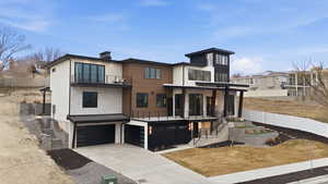 Back of house with a balcony, an attached garage, driveway, a standing seam roof, and a chimney