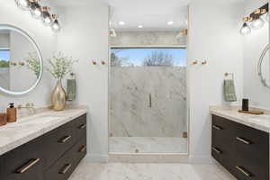 Full bath featuring two vanities, a marble finish shower, and recessed lighting