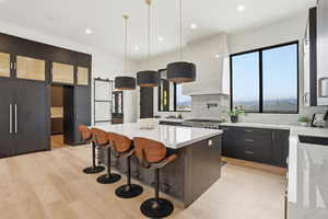 Two tone kitchen featuring a breakfast bar, a barn door, light stone countertops, a kitchen island, and hanging light fixtures