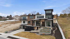 Modern home featuring concrete driveway, a balcony, a garage, and stone siding