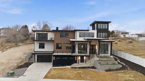 View of front facade featuring a balcony, driveway, a standing seam roof, an attached garage, and a patio