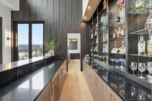 Bar area featuring dark stone countertops, light wood finished floors, beverage cooler, and modern cabinets