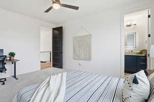 Bedroom with light colored carpet, a ceiling fan, connected bathroom, and an office area