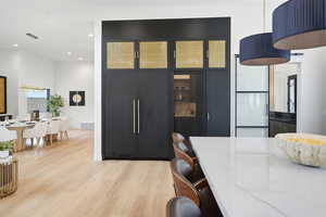 Kitchen featuring decorative light fixtures, a breakfast bar area, light wood finished floors, glass insert cabinets, and a high ceiling