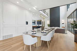 Dining room with a high ceiling, light wood-type flooring, a fireplace, a decorative wall, and recessed lighting
