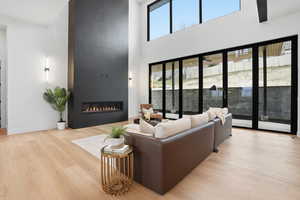 Living area with light wood finished floors, a fireplace, healthy amount of natural light, and a high ceiling