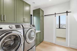 Laundry area featuring a barn door, light wood finished floors, washing machine and clothes dryer, and cabinet space