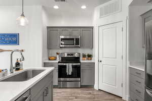 Kitchen featuring gray cabinets, stainless steel appliances, pendant lighting, light wood finished floors, and light stone counters