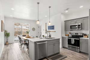 Kitchen featuring gray cabinetry, stainless steel appliances, light wood-style flooring, and an island with sink