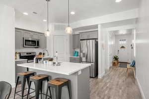 Kitchen with gray cabinets, stainless steel appliances, a kitchen bar, light wood-style floors, and hanging light fixtures