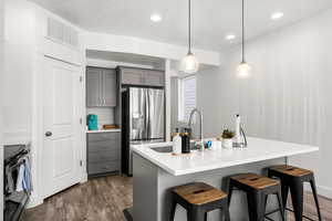 Kitchen featuring gray cabinetry, stainless steel appliances, pendant lighting, dark wood finished floors, and a breakfast bar