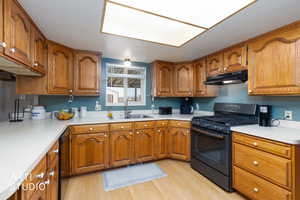 Kitchen with wood finish cabinetry, black appliances, light countertops, light wood finished floors, and a textured ceiling
