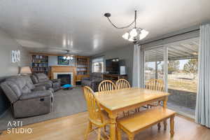 Dining space with a textured ceiling, a glass covered fireplace, wood finished floors, a ceiling fan, and suspended lighting