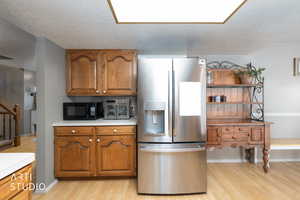 Kitchen with stainless steel refrigerator with ice dispenser, wood finish cabinetry, light countertops, a textured ceiling, and light wood finished floors