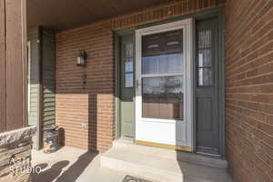 Doorway to property featuring brick siding and covered porch