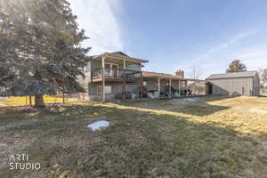 Back of property featuring a lawn, a patio, a deck, and an outbuilding