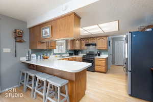 Kitchen with freestanding refrigerator, wood finish cabinetry, a breakfast bar, a peninsula, and gas stove