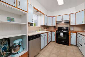 Dual tone kitchen featuring two tone cabinets, black gas range oven, stainless steel dishwasher, open shelves, and light countertops