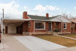 View of front of house with a chimney, brick siding, driveway, and a front yard