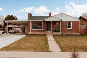 View of front of property with a chimney, brick siding, a front yard, concrete driveway, and a carport