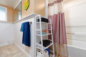 Full bathroom with a wainscoted wall, shower / bath combo, and light tile patterned floors
