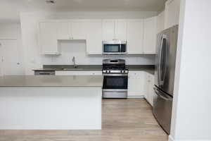 Kitchen with stainless steel appliances, white cabinetry, light wood-type flooring, and dark stone counters