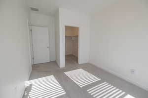 Unfurnished bedroom with a spacious closet and light colored carpet