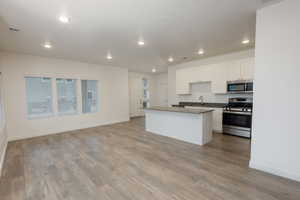 Kitchen with open floor plan, stainless steel appliances, white cabinets, dark countertops, and a center island