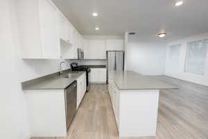 Kitchen with stainless steel appliances, white cabinets, light wood-style flooring, recessed lighting, and a kitchen island