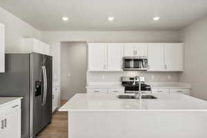 Kitchen featuring stainless steel appliances, white cabinets, a center island with sink, light stone counters, and light wood-type flooring