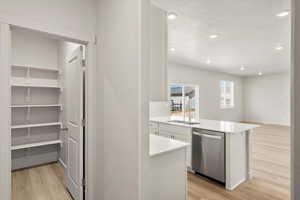 Kitchen featuring light wood finished floors, dishwasher, a peninsula, recessed lighting, and white cabinetry