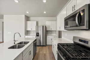 Kitchen featuring stainless steel appliances, light stone counters, white cabinetry, light wood finished floors, and recessed lighting