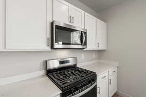 Kitchen with stainless steel appliances, light stone counters, and white cabinetry