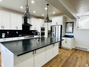 Kitchen with a center island with sink, light wood-type flooring, a textured ceiling, and white cabinetry