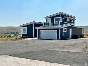 View of front of home with an attached garage, a mountain view, driveway, a metal roof, and a balcony