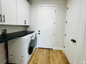 Laundry room featuring light wood-style flooring, cabinet space, and washing machine and dryer