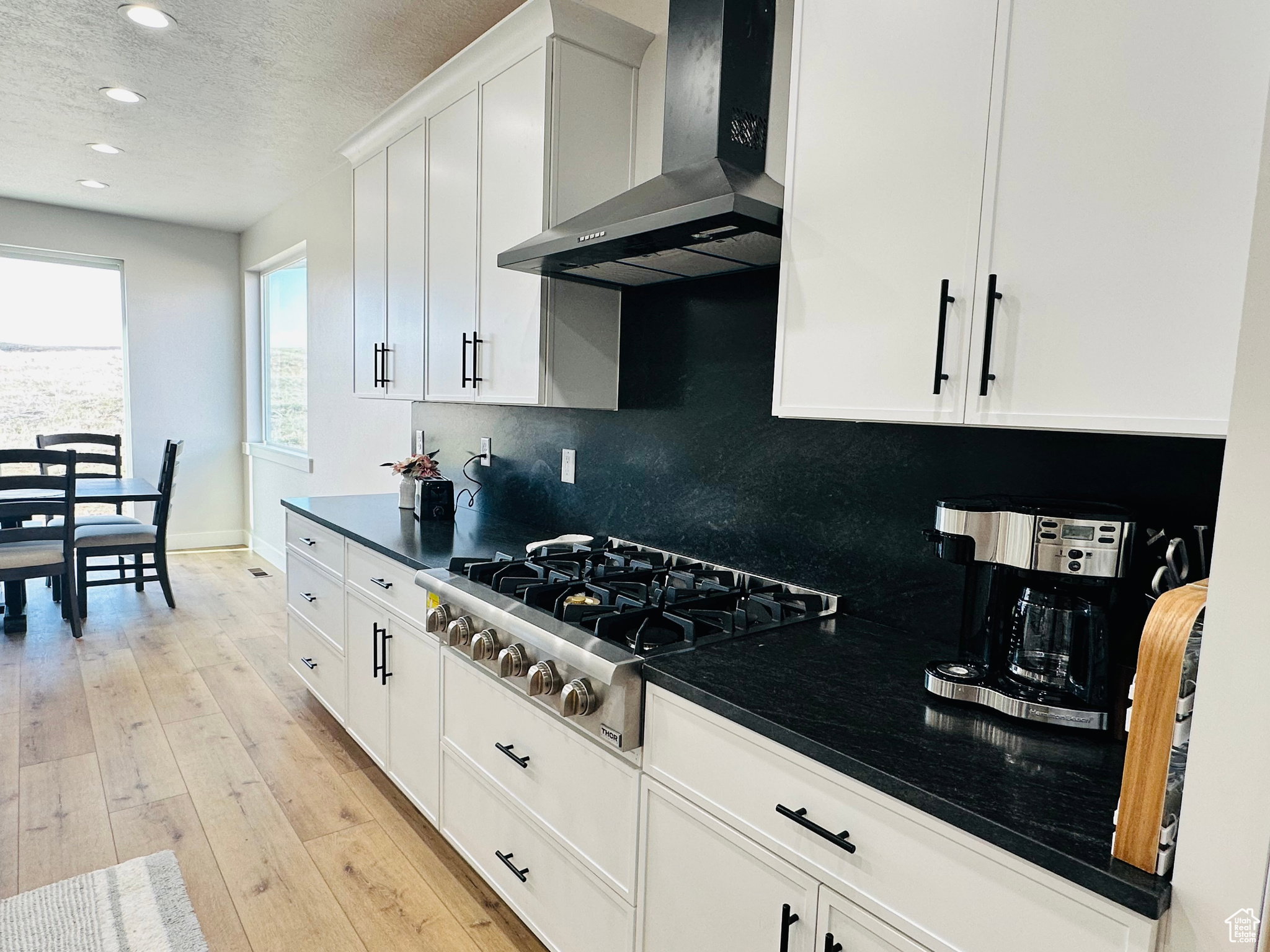 Kitchen featuring a textured ceiling, white cabinetry, stainless steel gas cooktop, light wood finished floors, and recessed lighting