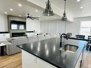 Kitchen with an island with sink, light wood finished floors, a fireplace, pendant lighting, and ceiling fan