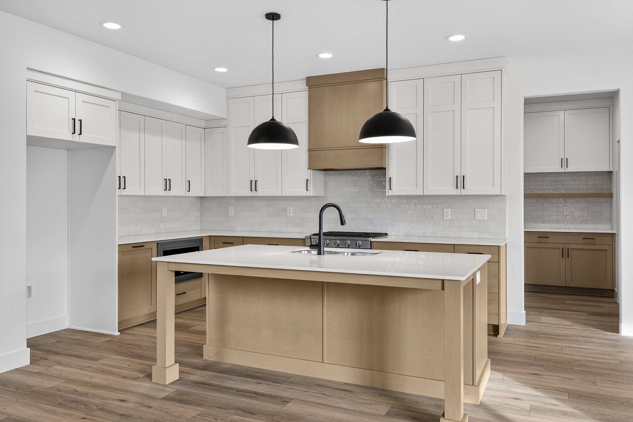 Kitchen with light wood-style floors, two tone cabinetry, an island with sink, decorative light fixtures, and a kitchen bar