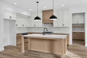 Kitchen with light wood-style floors, two tone cabinetry, an island with sink, decorative light fixtures, and a kitchen bar