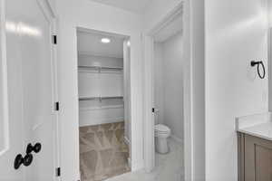 Bathroom featuring light marble finish flooring, a spacious closet, and vanity